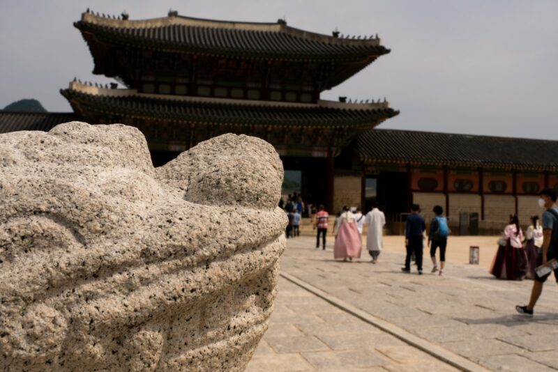 a stone statue in front of a building with a large stone wall